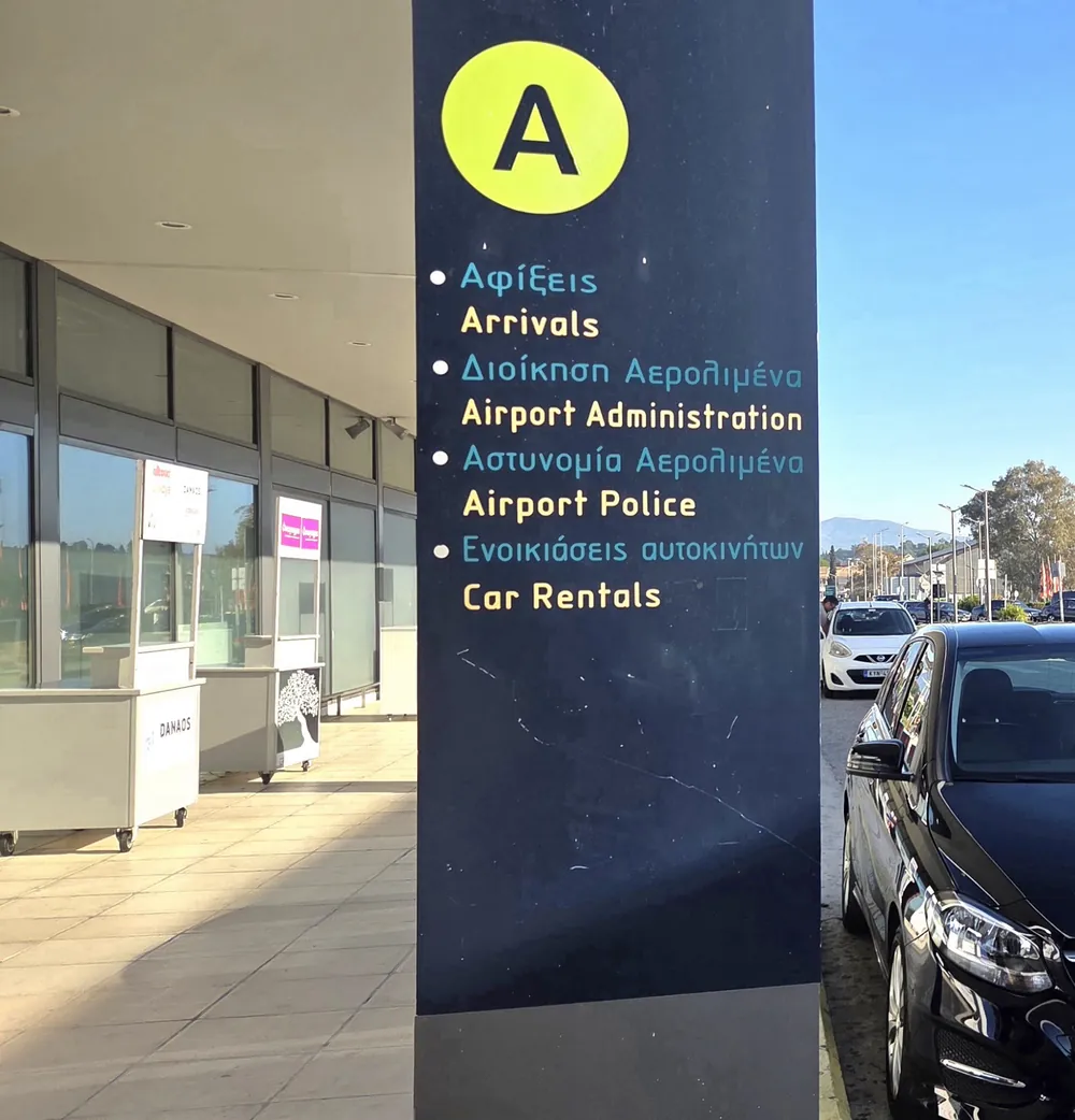 Arrivals sign at Corfu Airport, the car parked beside it